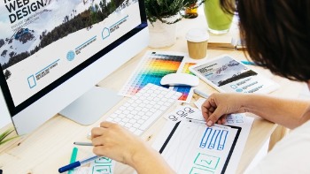 Person sitzt am am Desktop mit Skizzen und Farbschema zu Webdesign